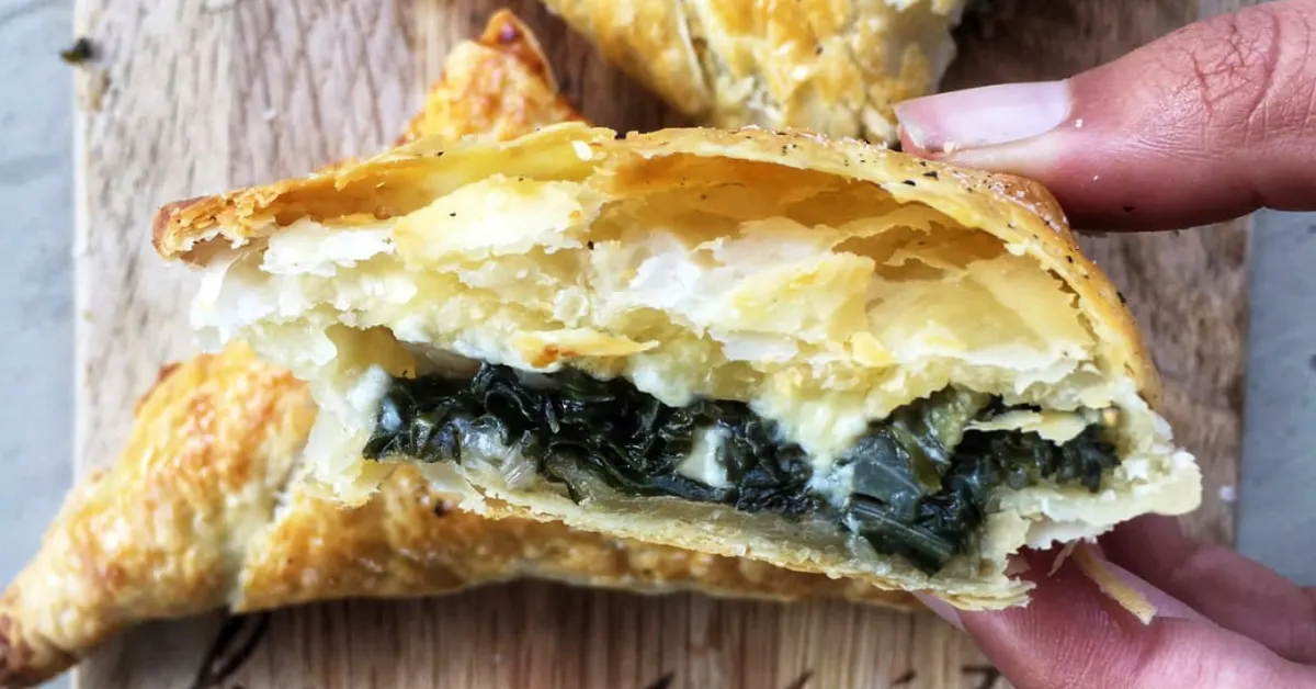 Flaky spinach pie slice with layers of spinach, mozzarella, and feta. Golden brown pastry, showcasing a delicious homemade spinach pie recipe.