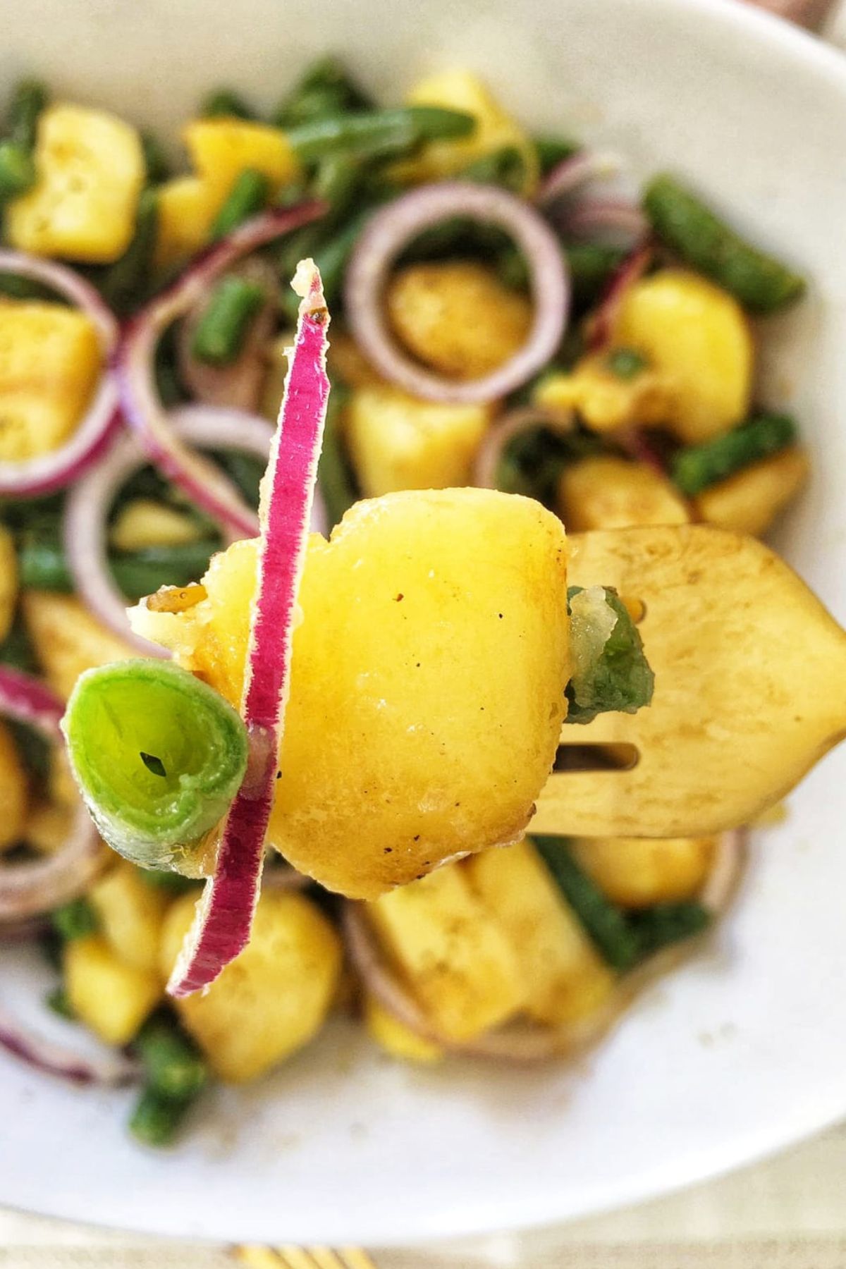 A fork holds a bite of Italian potato salad, one of many delicious Italian side dishes for Christmas. The salad includes potatoes, green beans, and red onion.