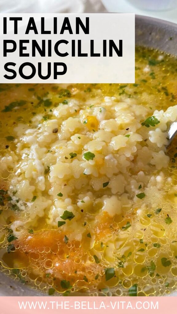 Close-up of Italian penicillin soup with star-shaped pasta, broth, carrots, and parsley. A spoonful is raised, showing the texture of this comforting soup. Text: Italian Penicillin Soup. www.the-bella-vita.com
