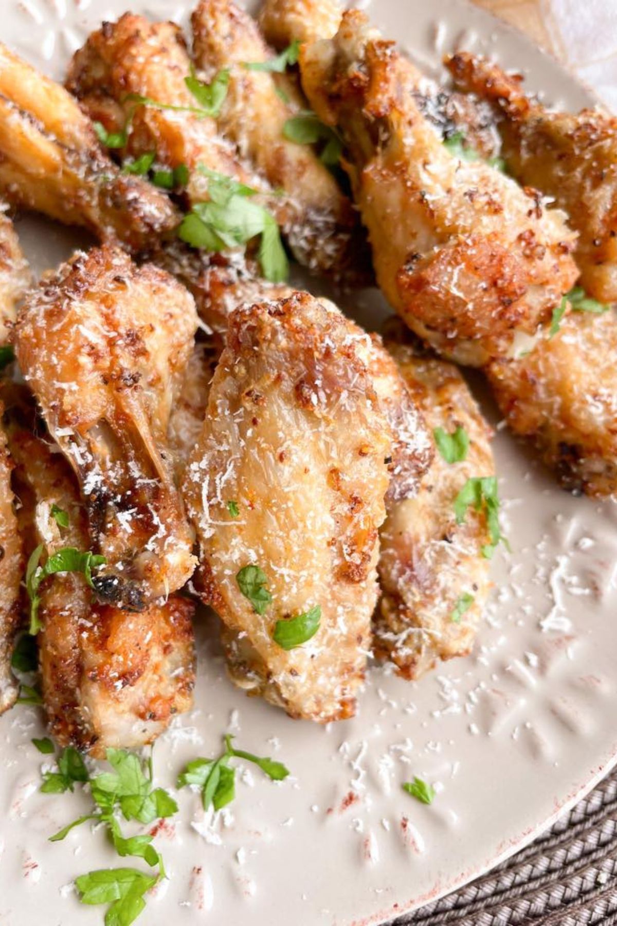 Crispy baked chicken wings, perfect for 30 minute meals, are piled on a plate and garnished with fresh parsley and grated Parmesan cheese.