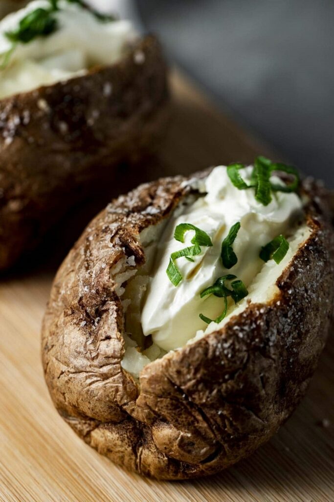 Baked potato topped with sour cream and chives on a wooden board.