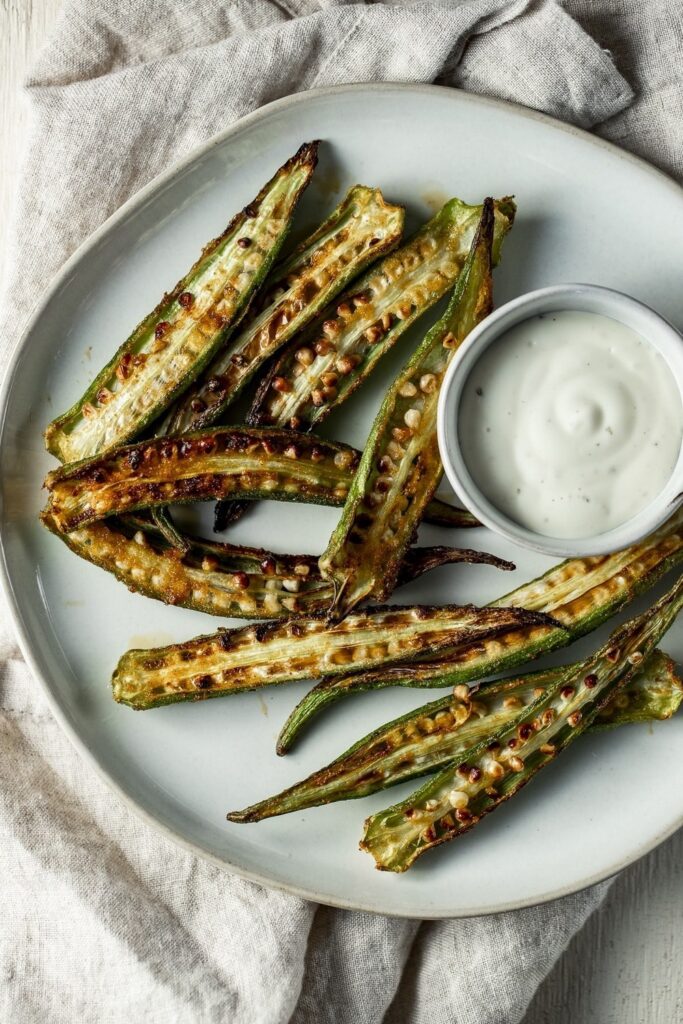 Crispy air-fried okra spears served with a creamy dipping sauce on a plate.