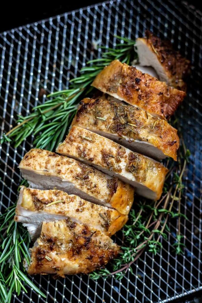 Sliced air fryer turkey breast with rosemary and thyme on a wire rack.