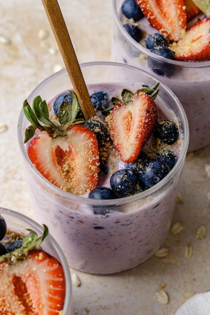 Berry Cheesecake Overnight Oats Overnight oats recipe in glass with blueberries, strawberries, and a wooden spoon.