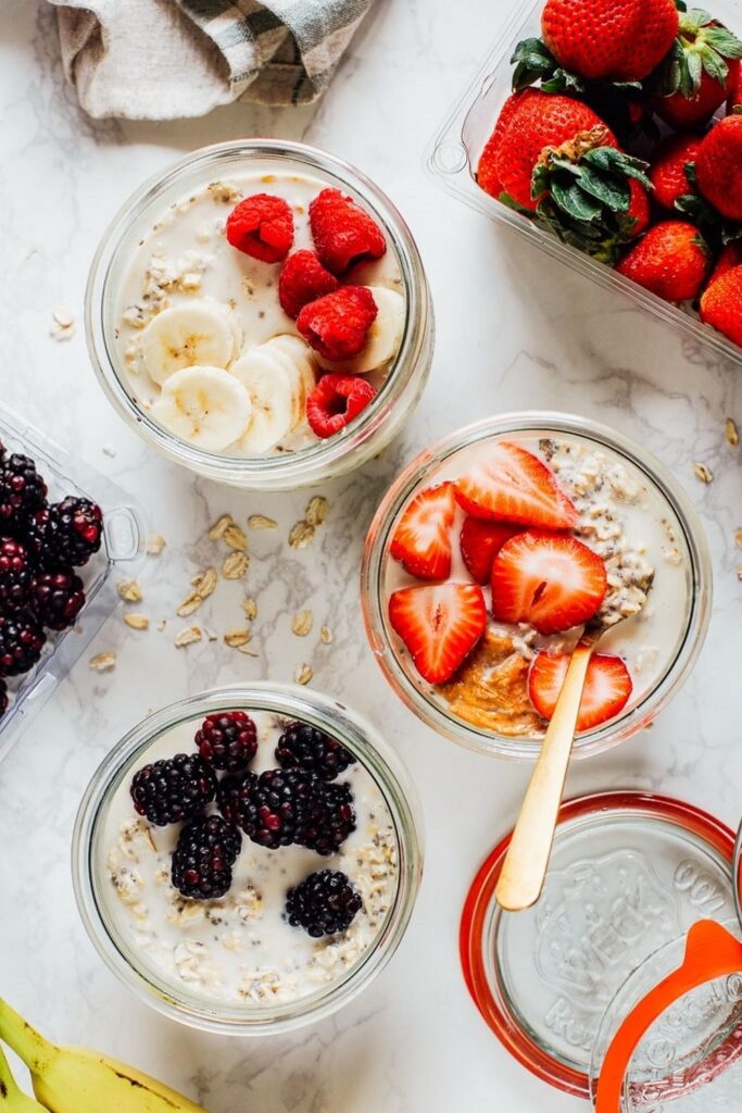High Protein Overnight Oats Without Yogurt Three jars of overnight oats recipes with fruit toppings: strawberries, blackberries, raspberries, and bananas.