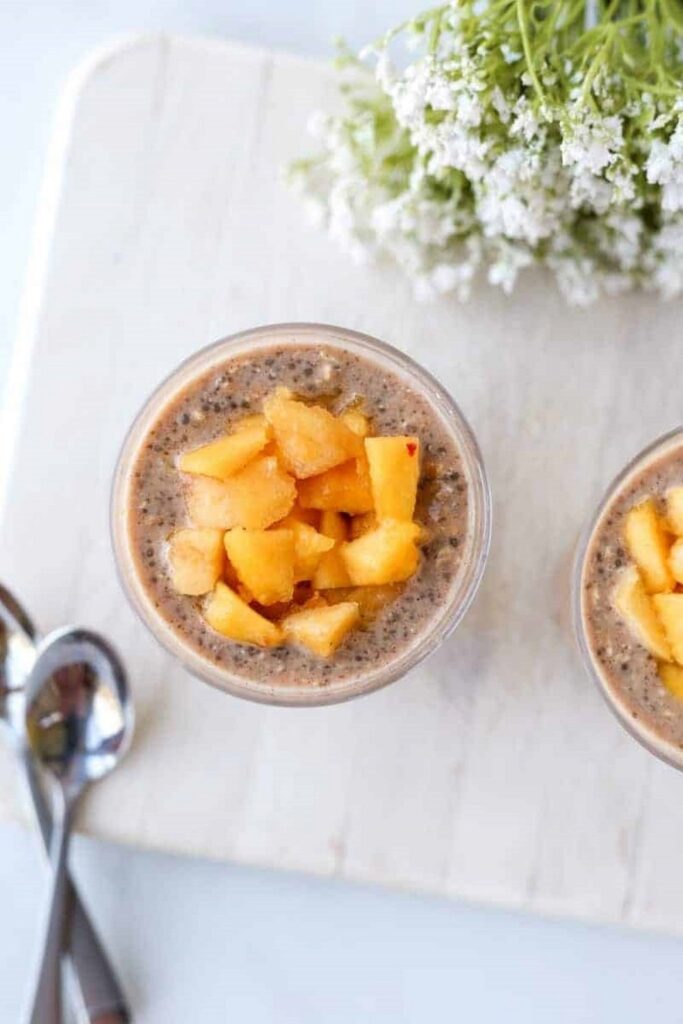 Peach Pie Overnight Oats Overnight oats recipe with diced peaches in a glass on a white board.