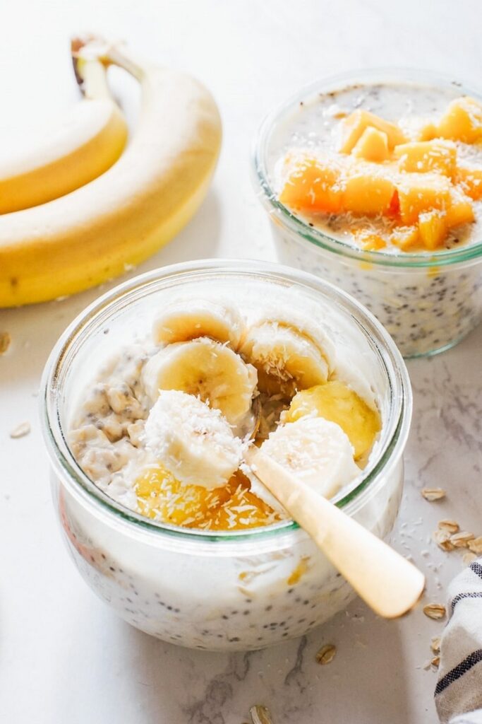 Tropical Overnight Oats With Coconut Milk Overnight oats recipes: Two glass jars filled with overnight oats topped with banana and mango.
