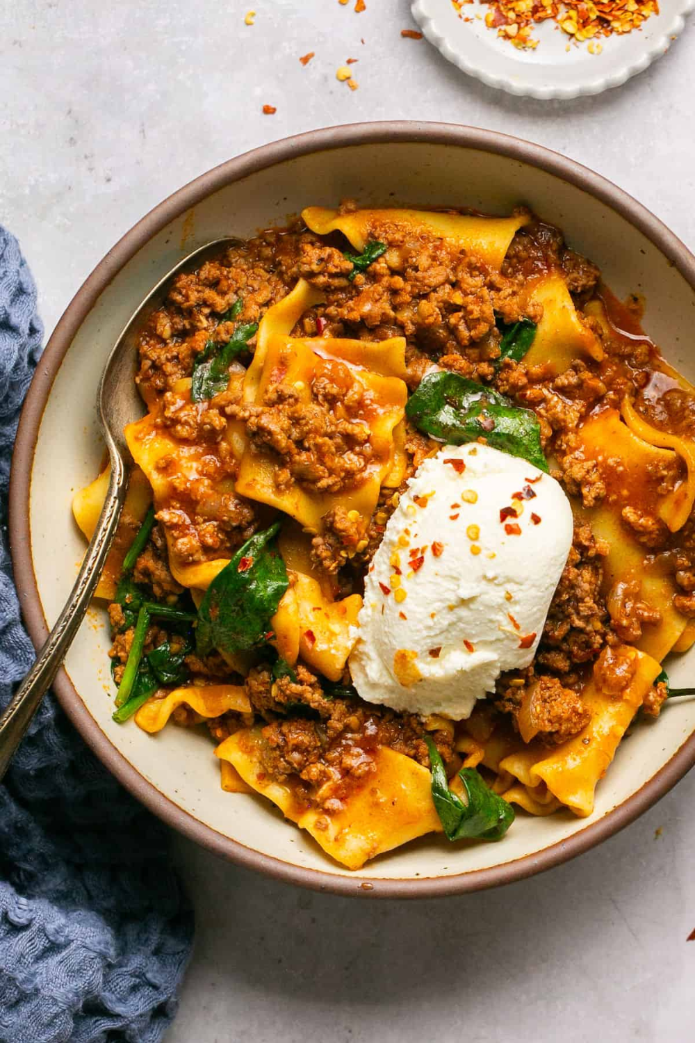 A bowl of slow cooker Italian pasta with meat sauce, spinach, and a dollop of ricotta cheese. A delicious example of Italian slow cooker recipes.