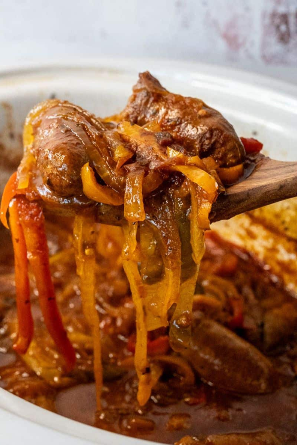 Spoonful of slow cooker sausage and peppers dripping with savory sauce. This easy Italian slow cooker recipe features browned sausages, bell peppers, and onions cooked to perfection.