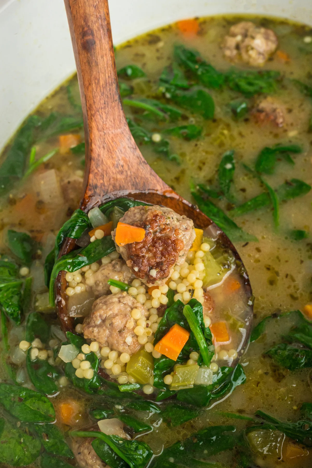 Spoonful of Italian Wedding Soup featuring meatballs, spinach, pasta, carrots, and broth. Perfect for slow cooker recipes and a comforting meal.