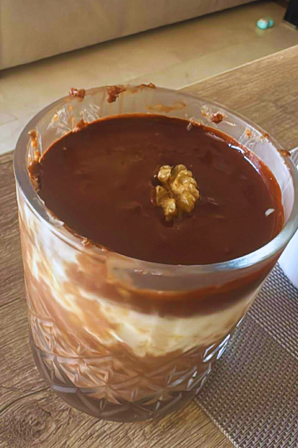 Glass of chocolate oatmeal topped with walnut on a wooden table