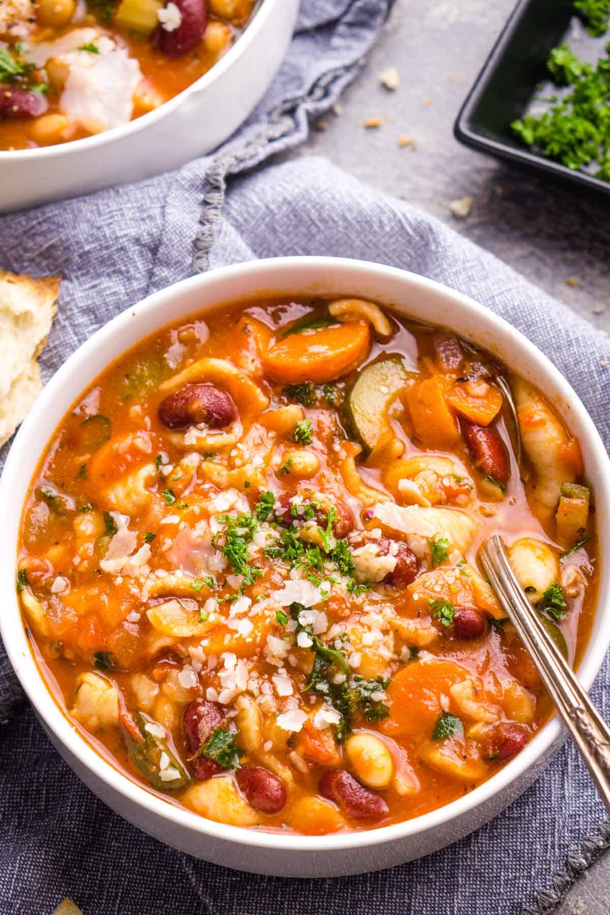 A bowl of hearty vegan Italian soup, showcasing a mix of colorful vegetables, beans, and pasta, topped with vegan parmesan and fresh herbs. One of many delicious vegan Italian recipes.