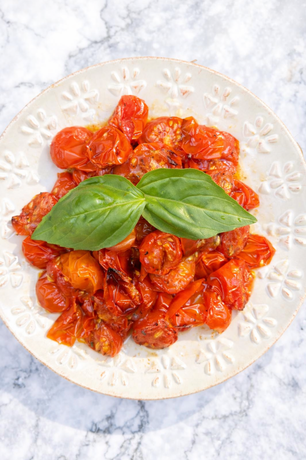 Air fryer roasted tomatoes on a decorative white plate, garnished with fresh basil. The tomatoes are vibrant red and caramelized, showcasing a simple, healthy side dish.