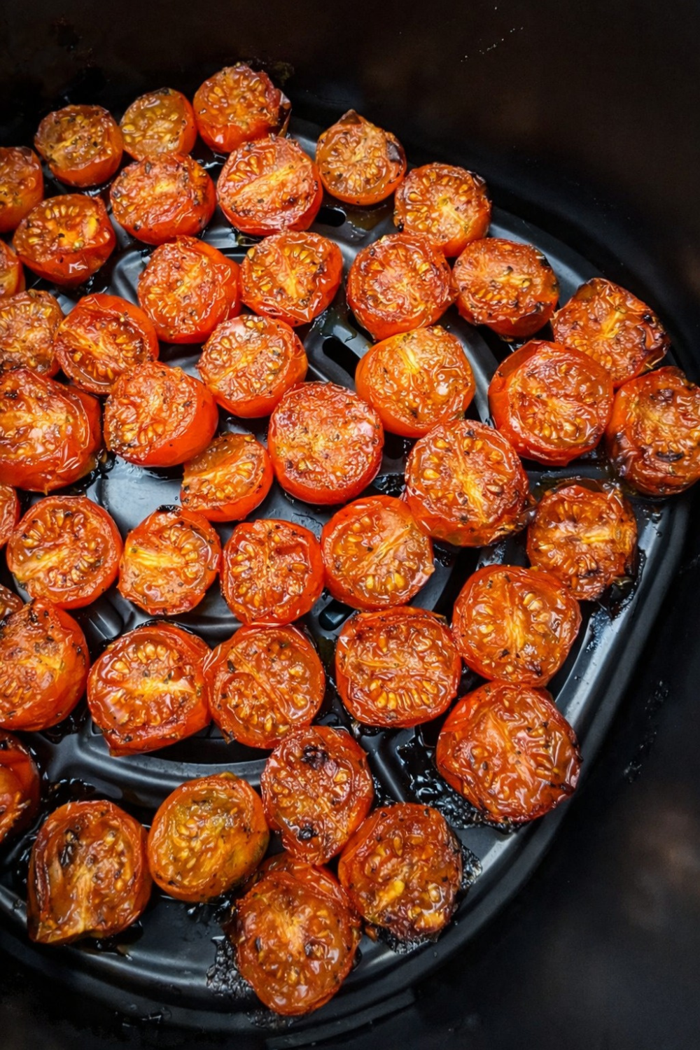 Air fryer basket filled with halved, roasted tomatoes. These juicy, perfectly cooked air fryer tomatoes are an easy recipe ready in minutes.