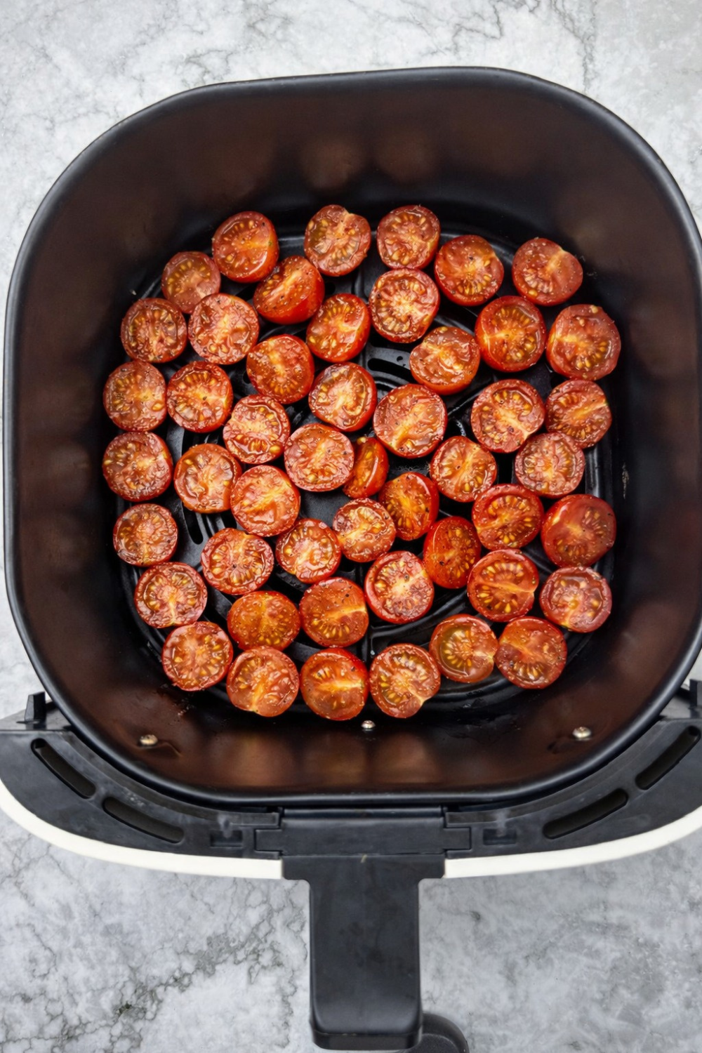 Air fryer cherry tomatoes, halved and roasted in the air fryer basket. These blistered tomatoes are bright red and ready to be used in a variety of recipes.