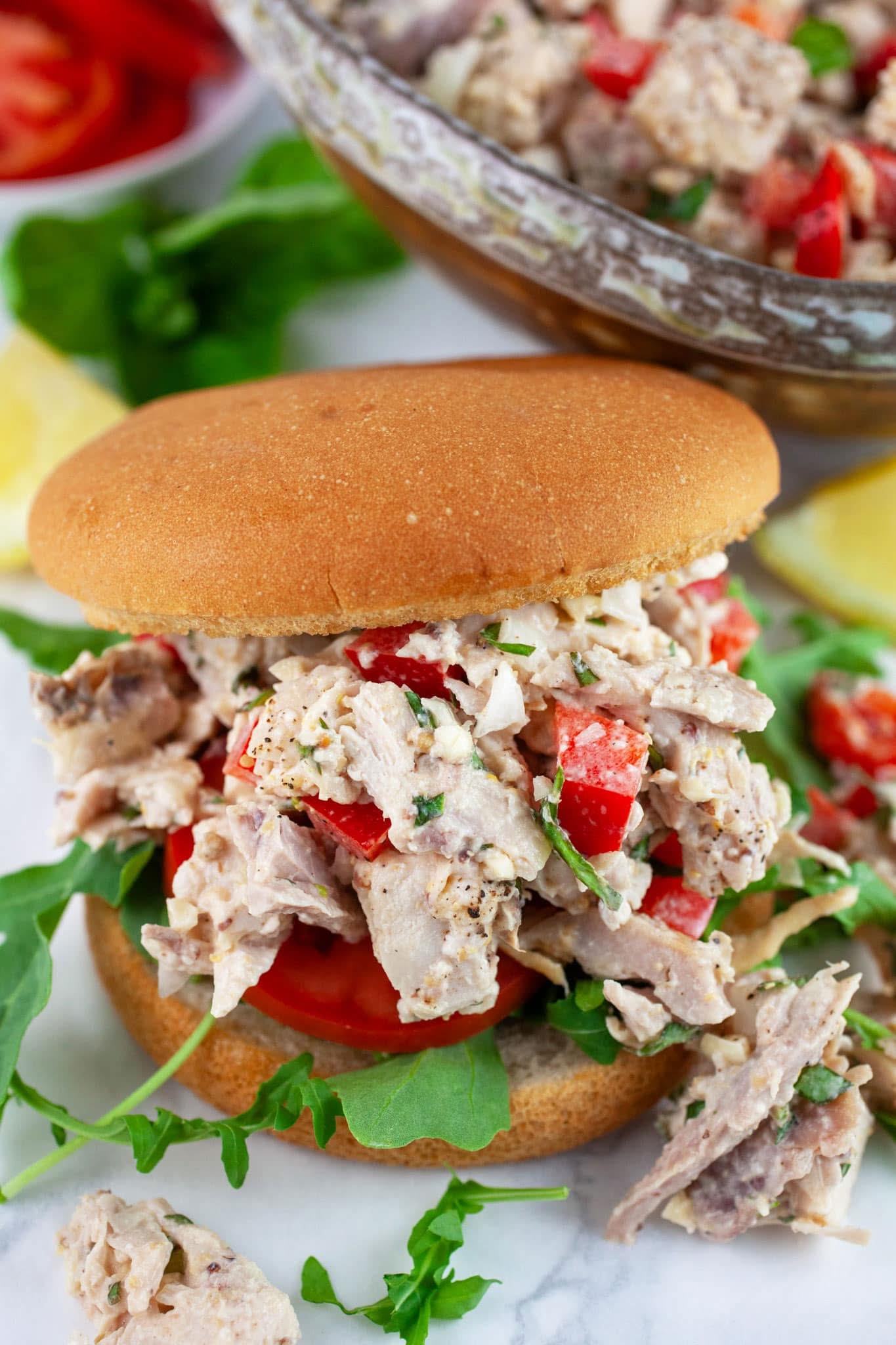 Close-up of a delicious chicken salad sandwich on a toasted bun, layered with fresh tomatoes, peppery arugula, and a creamy, herb-flecked chicken salad. This is a great example of a fresh basil recipe.