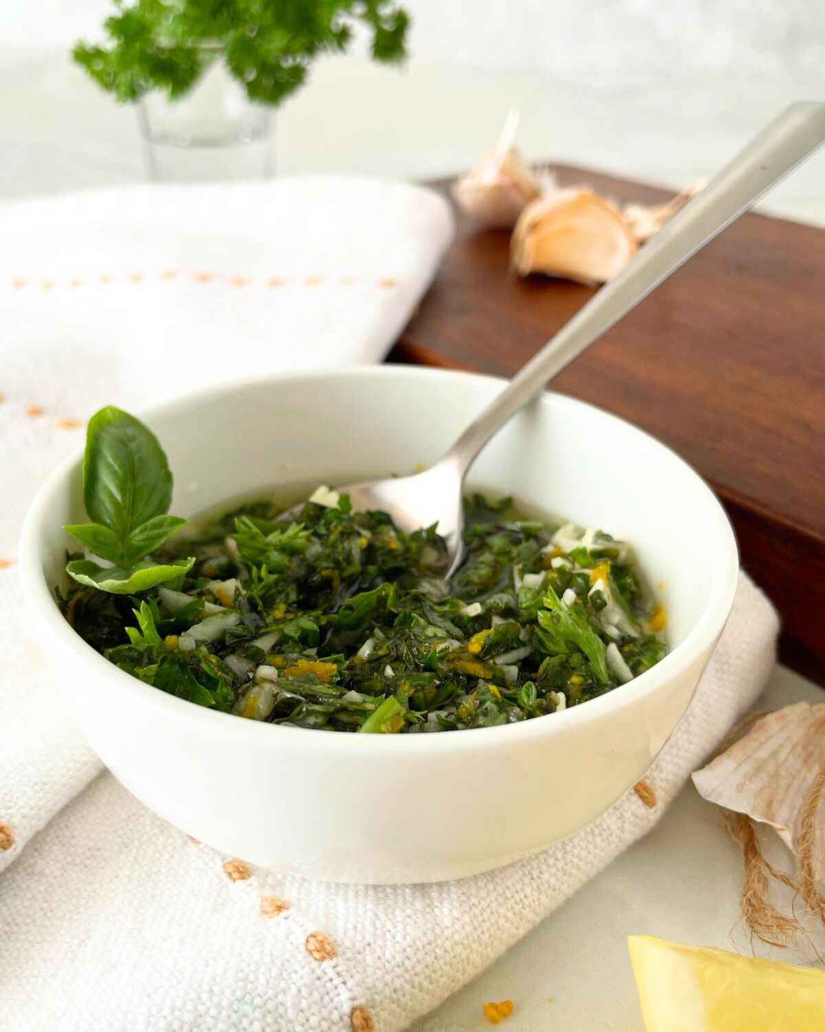 A vibrant bowl of fresh basil pesto, garnished with a basil leaf, sits on a white cloth. Garlic and lemon are visible in the background, hinting at ingredients for this fresh basil recipe.