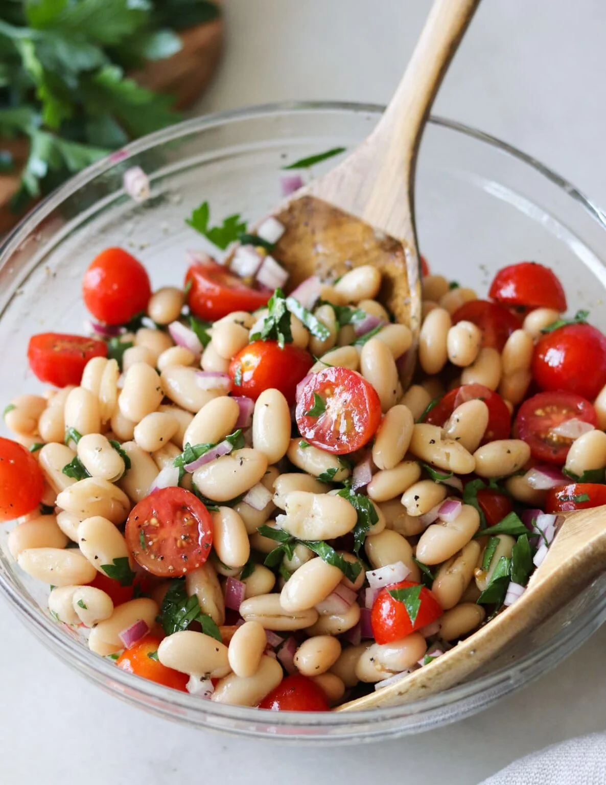 A refreshing Italian gluten-free white bean salad with cherry tomatoes, red onion, and parsley in a clear bowl, ready to be served.