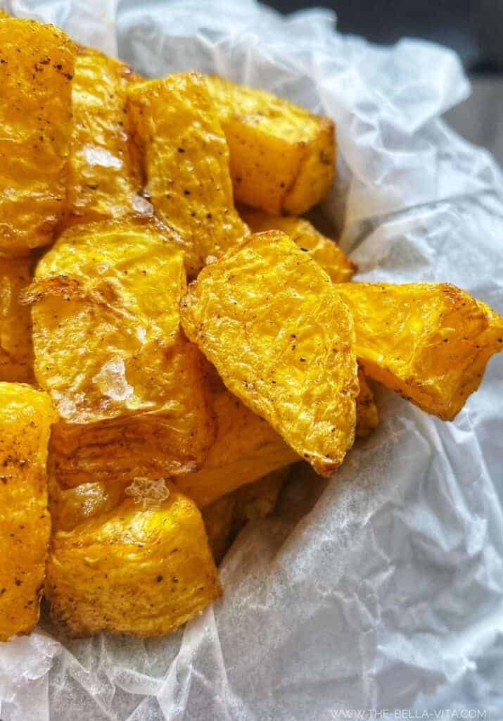 Golden air fryer butternut squash cubes, seasoned and ready to eat. Close-up shot of this easy air fryer butternut squash recipe served in a white paper container.