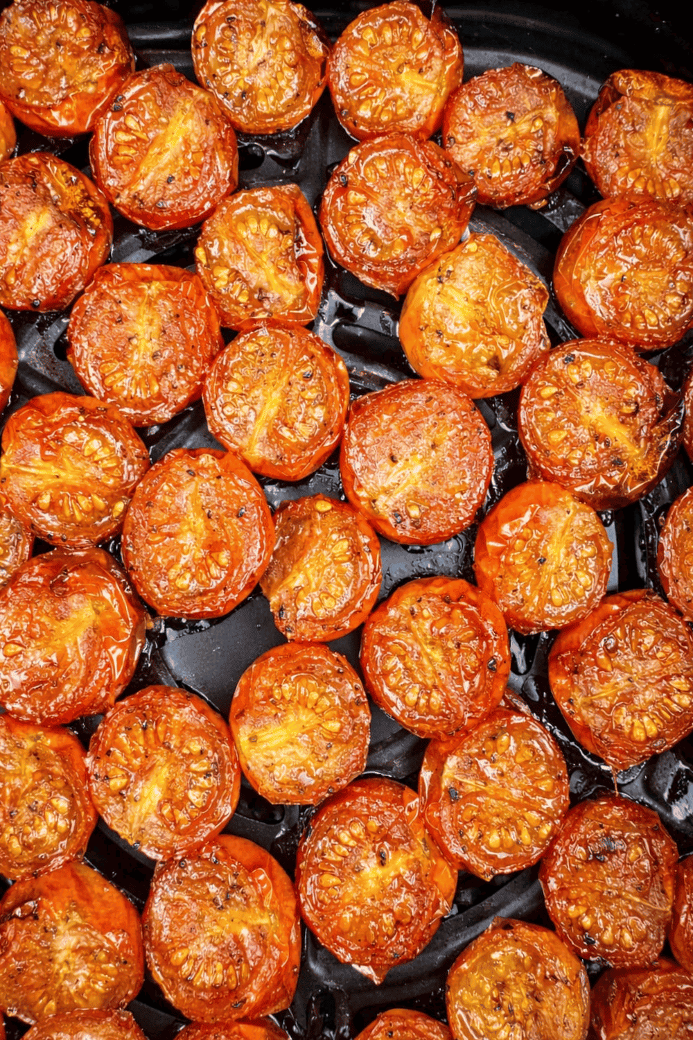 Close-up of roasted cherry tomato halves in an air fryer basket, caramelized and glistening.